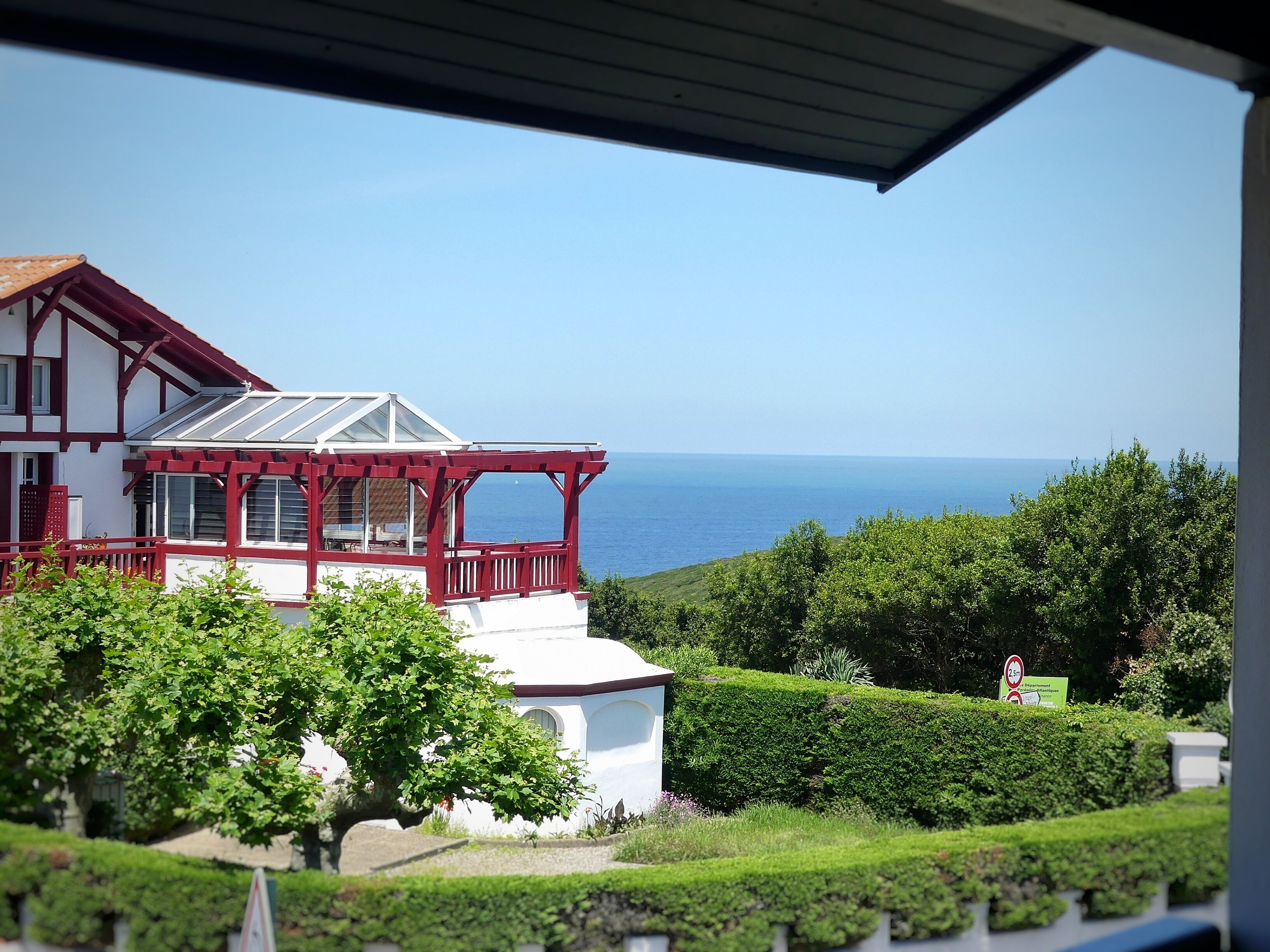 A two-story house with a red balcony, a white exterior, and a view of the sea.