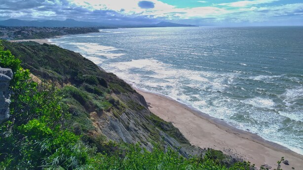 Eine Küstenlandschaft mit Strand, Klippen und einer fernen Bergkette.