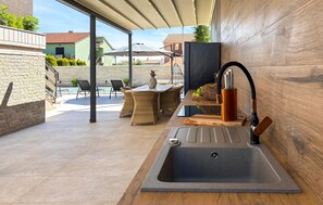 Eine moderne Außenküche mit Spüle, ein Essbereich mit Korbmöbeln und eine überdachte Terrasse.