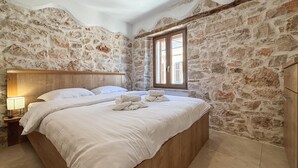 Une chambre avec un mur en pierre, une tête de lit en bois, un lit avec du linge de lit blanc et une table de chevet avec une lampe.