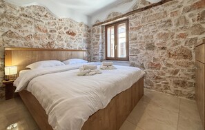 Ein Schlafzimmer mit Steinsandsteinwand, einem Holzkopfteil, einem Bett mit weißen Leinen und einem Nachttisch mit Lampe.