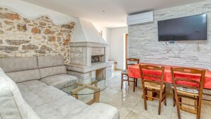 Un salon avec un mur en pierre, une cheminée, un canapé, une table basse en verre et un coin repas avec une nappe rouge.