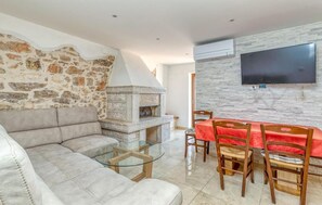 Ein Wohnzimmer mit Steinwand, Kamin, einer Couch, einem Glastisch und einem Essbereich mit roter Tischdecke.
