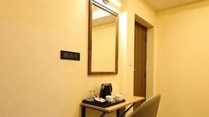 Quarto de hotel com escrivaninha, cafeteira, xícara e bandeja com objetos.