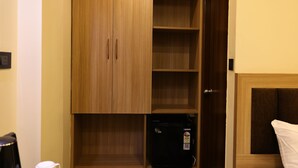 Quarto com guarda-roupa de madeira, frigorífico preto e cama branca.