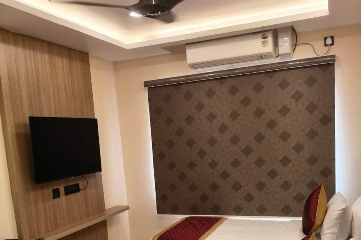 A hotel room with two beds, a ceiling fan, an air conditioning unit, a flat-screen TV, and a patterned headboard.