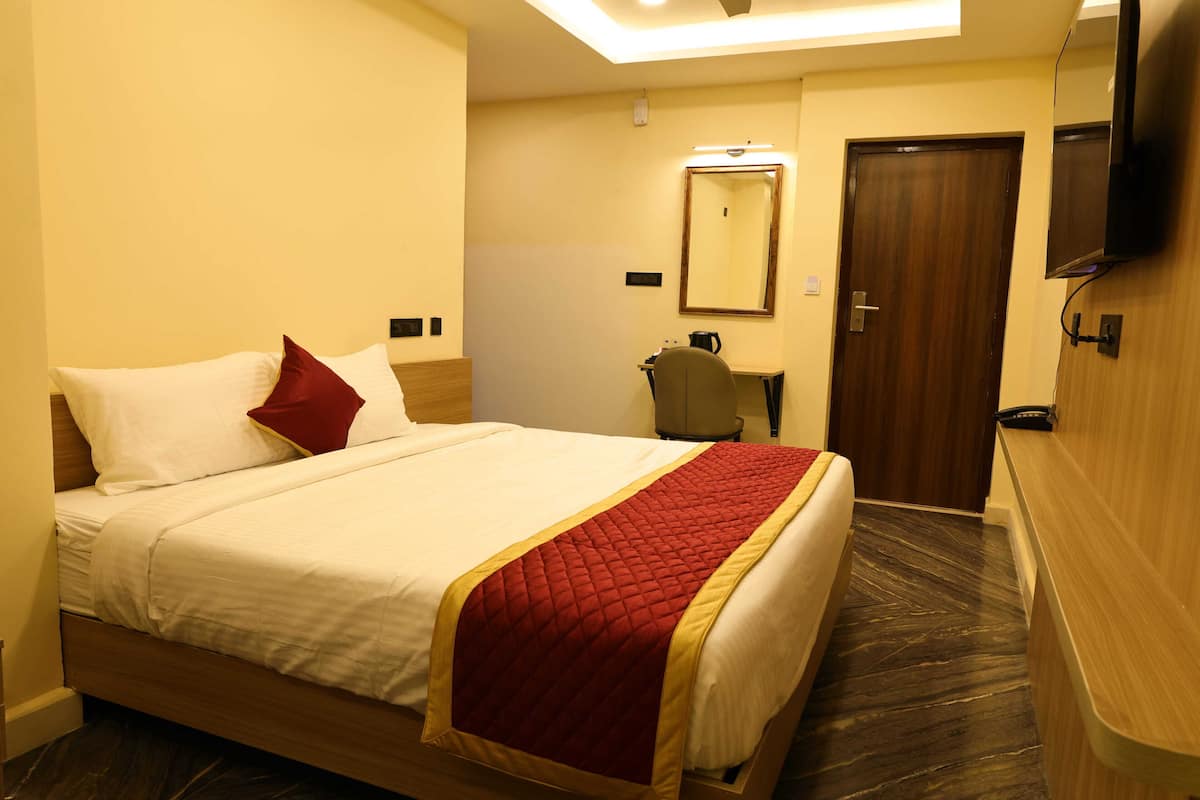 A hotel room with a bed, a desk, a chair, a mirror, and a television.