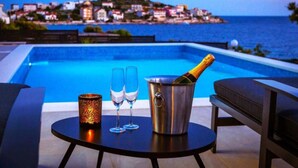 Escena junto a la piscina con vistas a un pueblo costero, una botella de champán, dos copas y un candelabro.