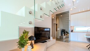 A modern living room with a flat-screen TV, a glass staircase, and a kitchen area. - Villa Nexia (Sibenik)