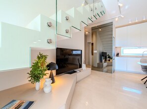 Ein modernes Wohnzimmer mit Flachbildfernseher, einer Glasstiege und einer Küchenzeile.