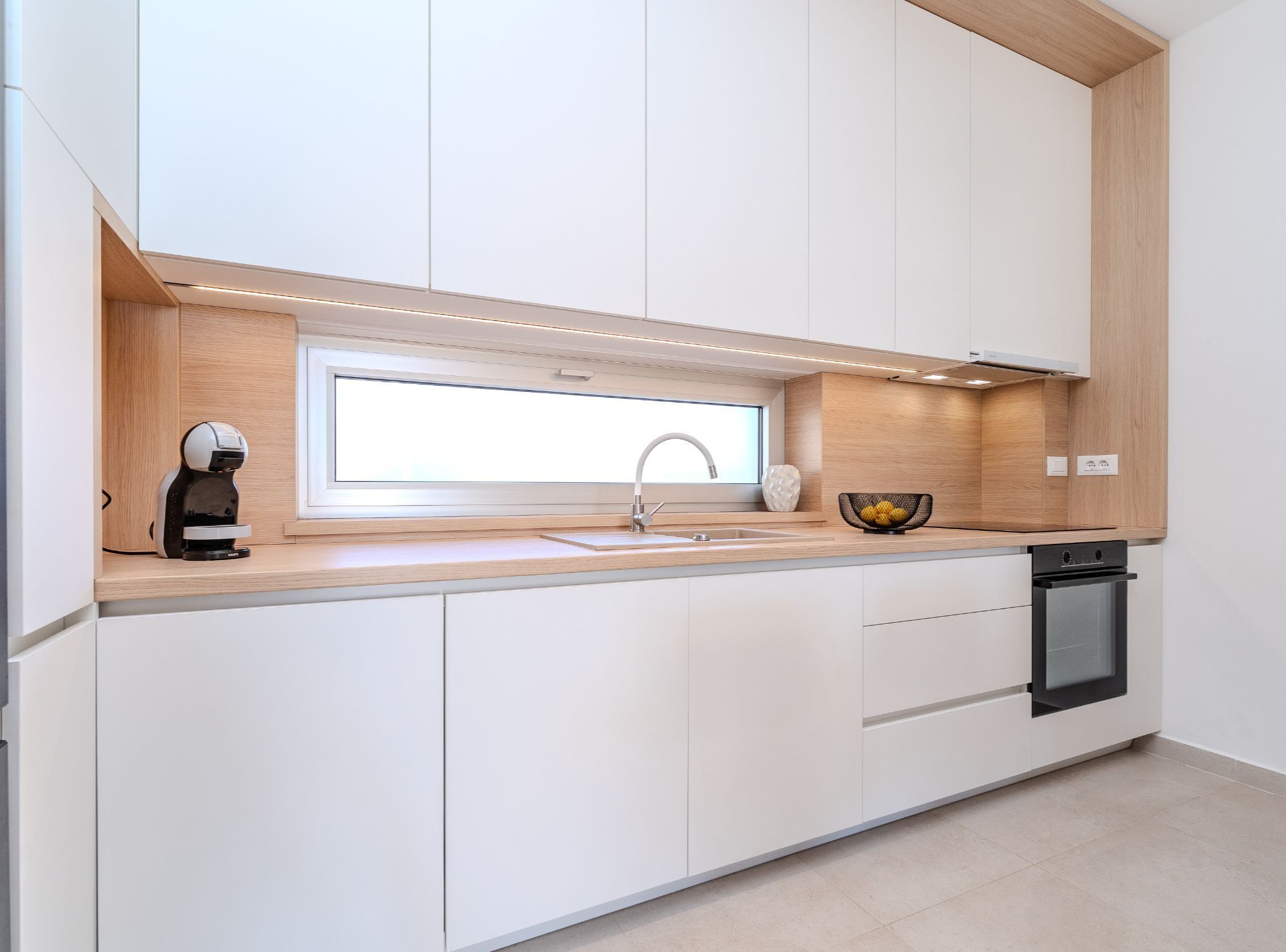 Una cocina moderna con lavavajillas incorporado, ventana sobre el fregadero y cafetera en la encimera.