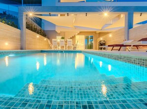 Ein Pool mit gefliestem Boden, umgeben von Liegestühlen und einem überdachten Sitzbereich.