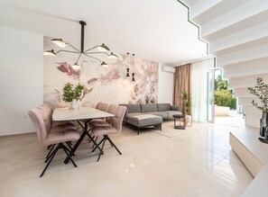 Ein modernes Wohnzimmer mit Essbereich, einer Couch, einem Couchtisch und einer Wand mit floralem Wandbild.
