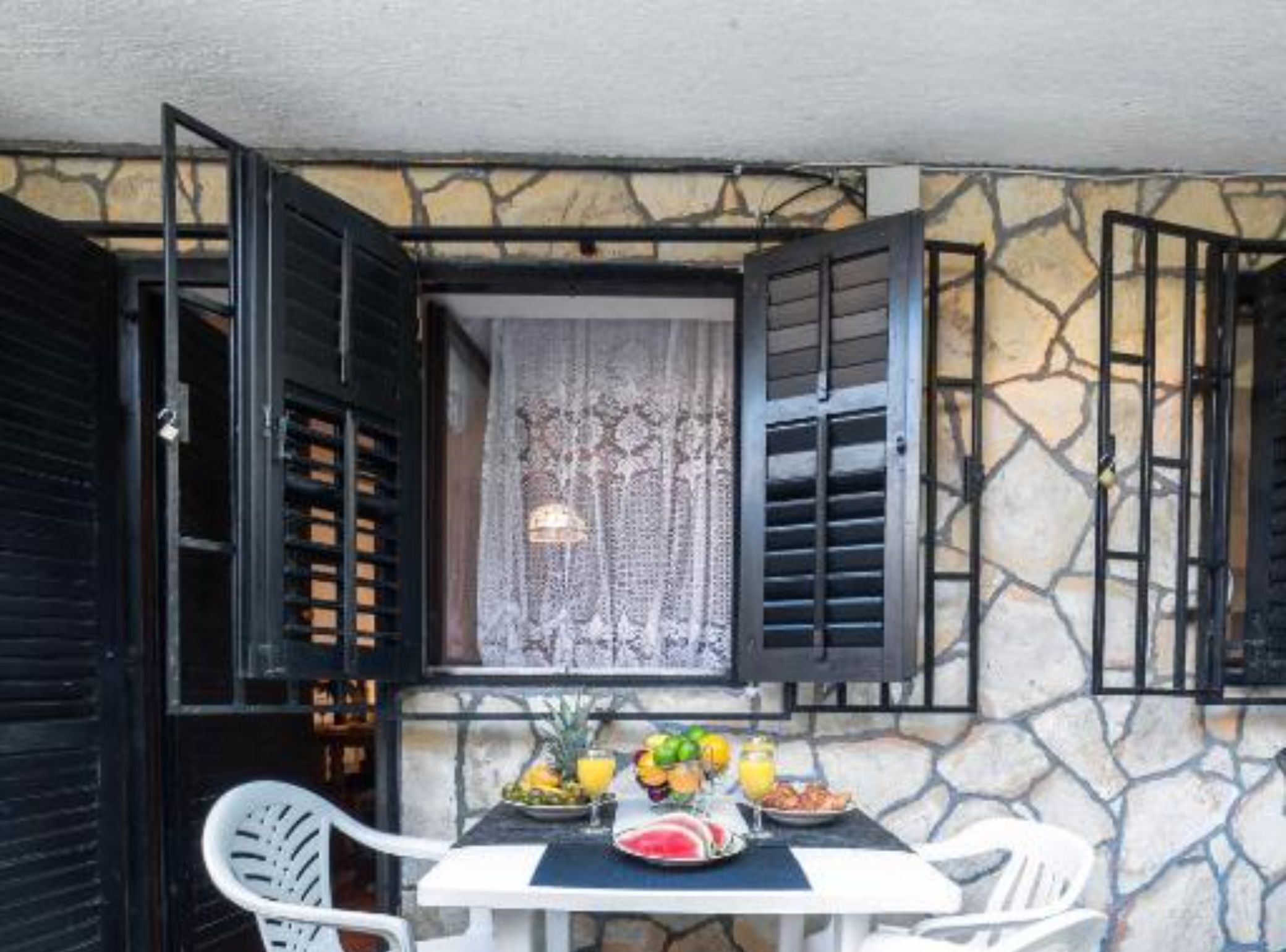 Una mesa preparada para el desayuno, una ventana con cortinas de encaje y una pared de piedra.