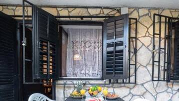 Una mesa preparada para el desayuno, una ventana con cortinas de encaje y una pared de piedra.