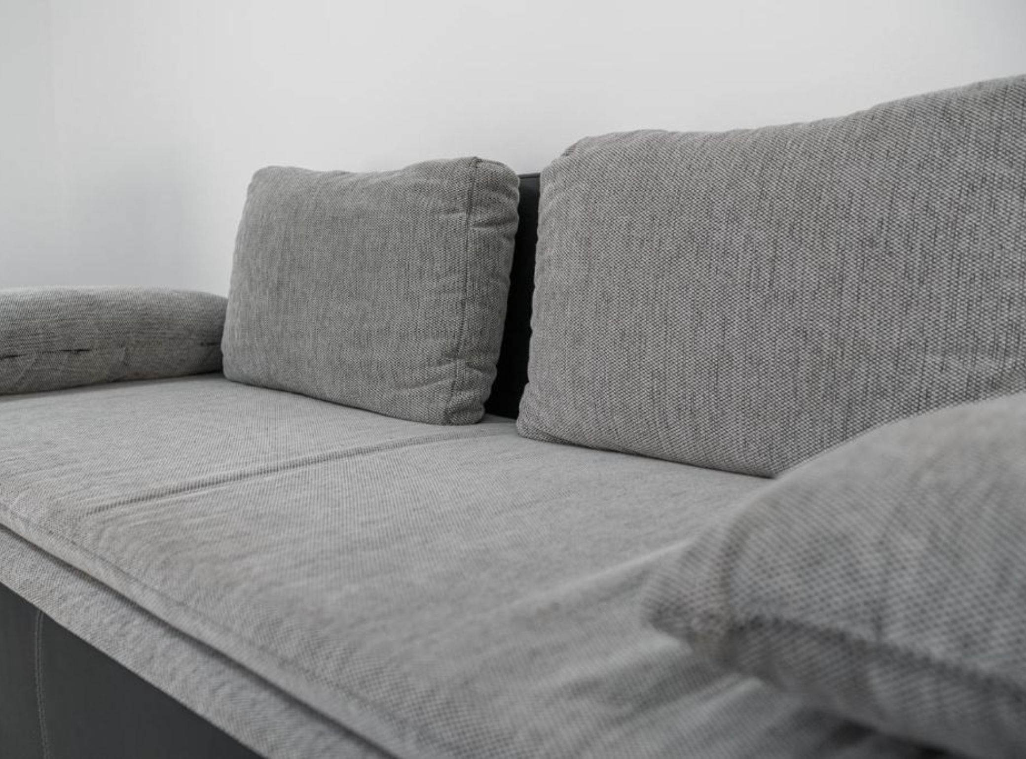 Un canapé gris, recouvert d’un tissu texturé, agrémenté d’un coussin noir.