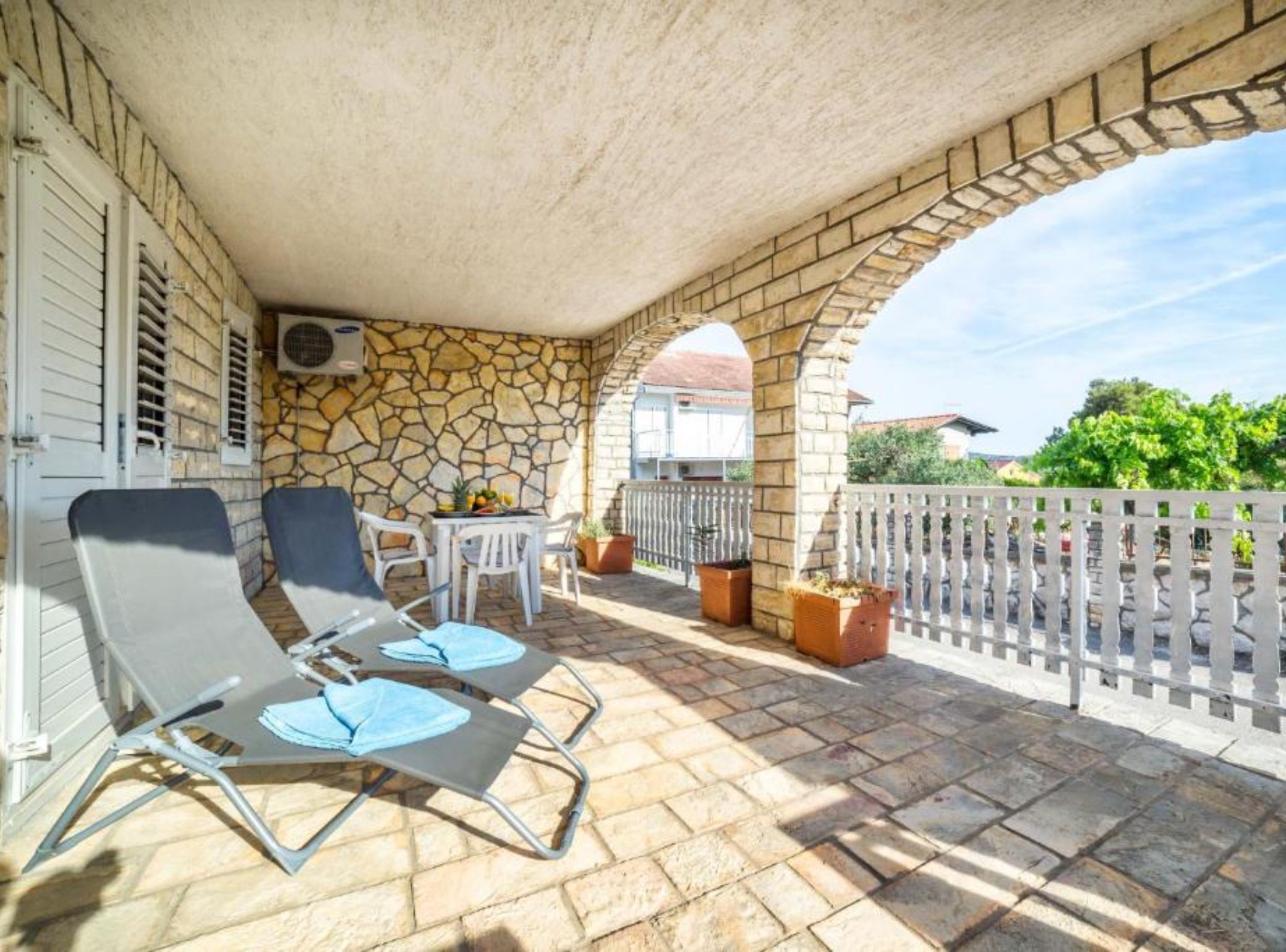 A covered outdoor area with stone walls, a white fence, and two lounge chairs.