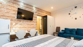Ein modernes Hotelzimmer mit Backsteinwand, Flachbildfernseher, einem Bett mit gemusterten Bettwäsche, einem blauen Sofa und einem Schreibtisch mit Stühlen.