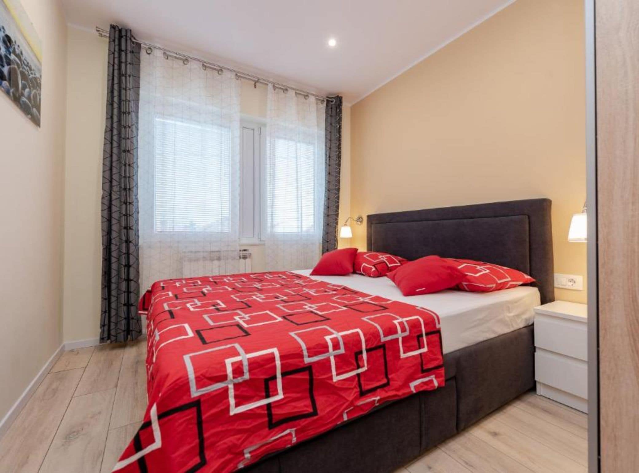 Une chambre à coucher avec un lit, des rideaux, une table de chevet et une lampe fixée au mur.
