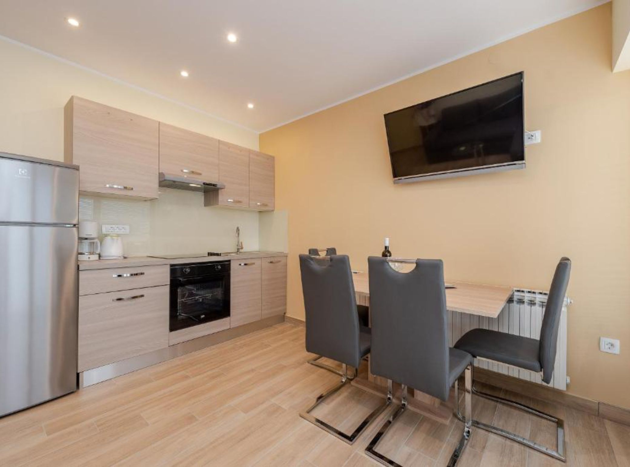A modern kitchen with a built-in oven, a refrigerator, and a dining area with a table and chairs.