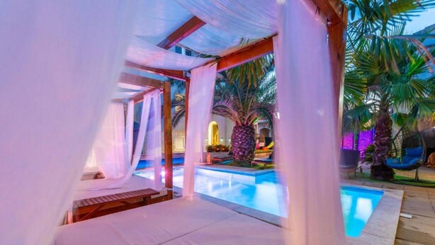 Área privativa de piscina com toldo, espreguiçadeiras e jardim tropical.
