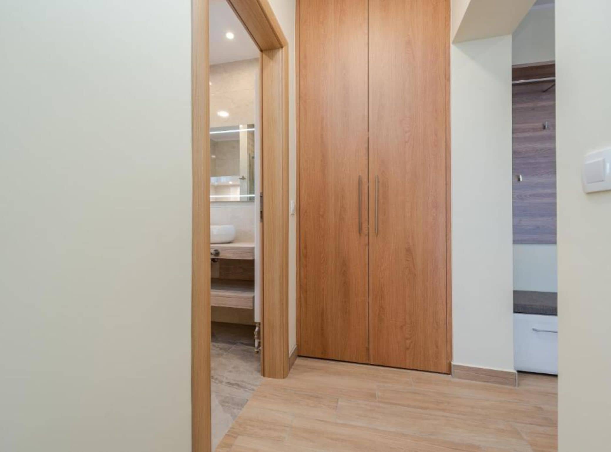 A hallway with a wooden wardrobe, a bathroom with a white sink, and a light switch on the wall.