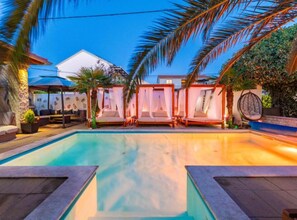 A swimming pool with a clear blue water surface, surrounded by lounge chairs and a covered seating area. - Bračić Premium Apartments With Outdoor Pool and Sauna (Sukosan)
