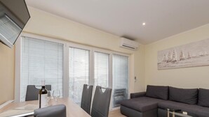 Uma sala de estar moderna com área de jantar, janelas amplas com persianas, um sofá cinza e um quadro na parede.