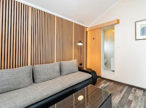 Habitació moderna amb sofà, taula de cafè de vidre, parets d'estriades de fusta, una porta de fusta i un quadre encimbellat a la paret.