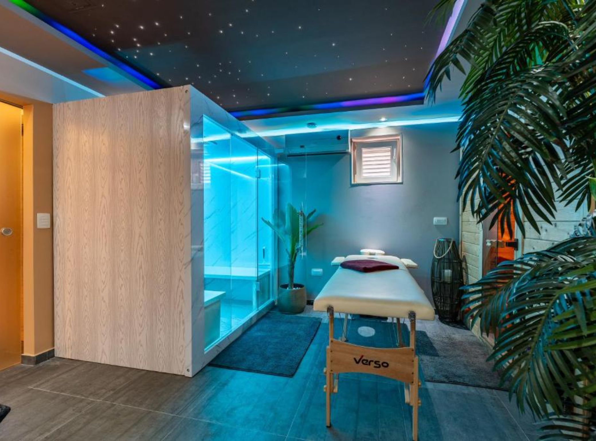 A room with a massage table, a wooden cabinet, a glass partition, and a ceiling with a starry design.