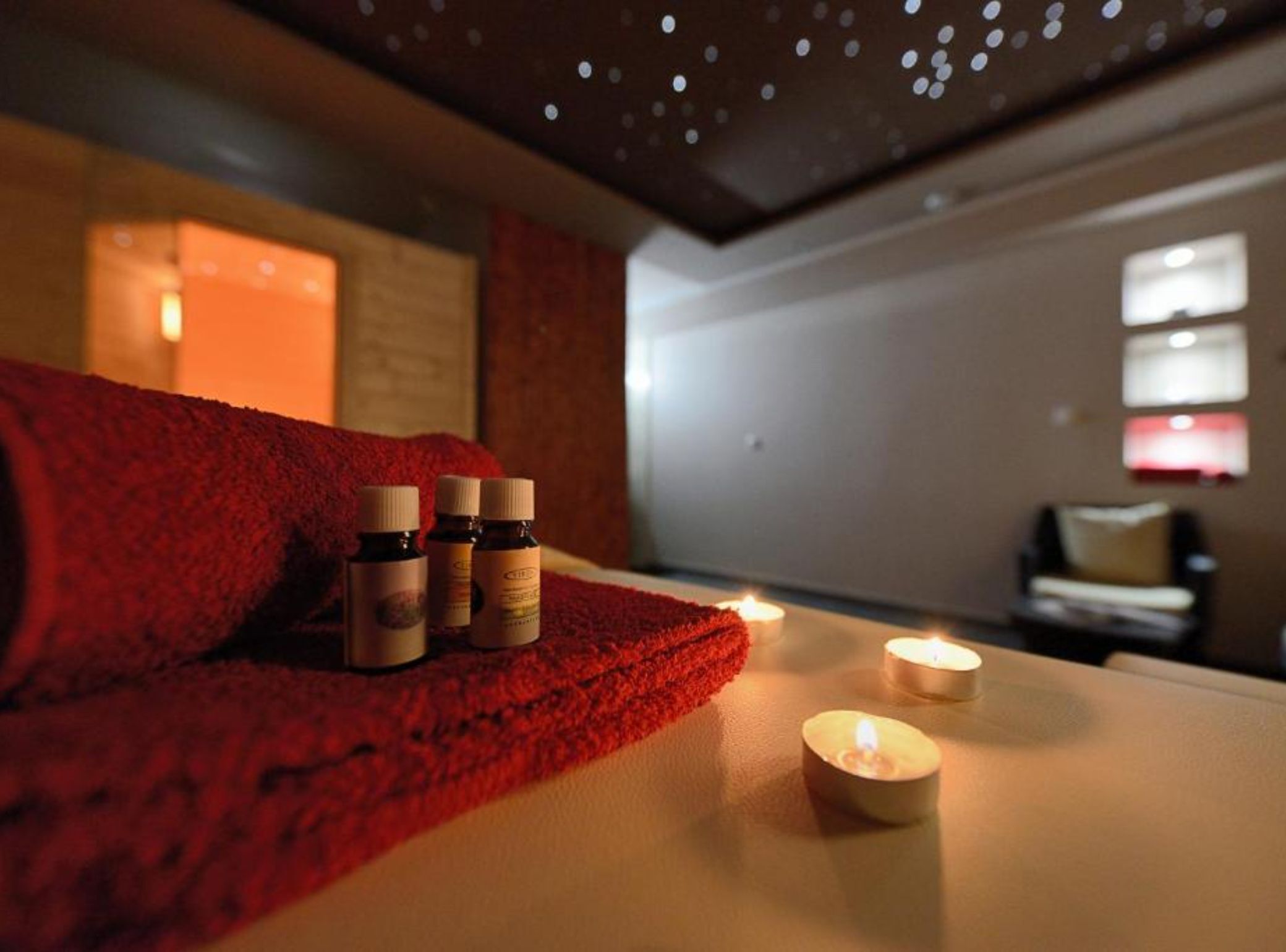 A spa room with a red towel, candles, and essential oil bottles.