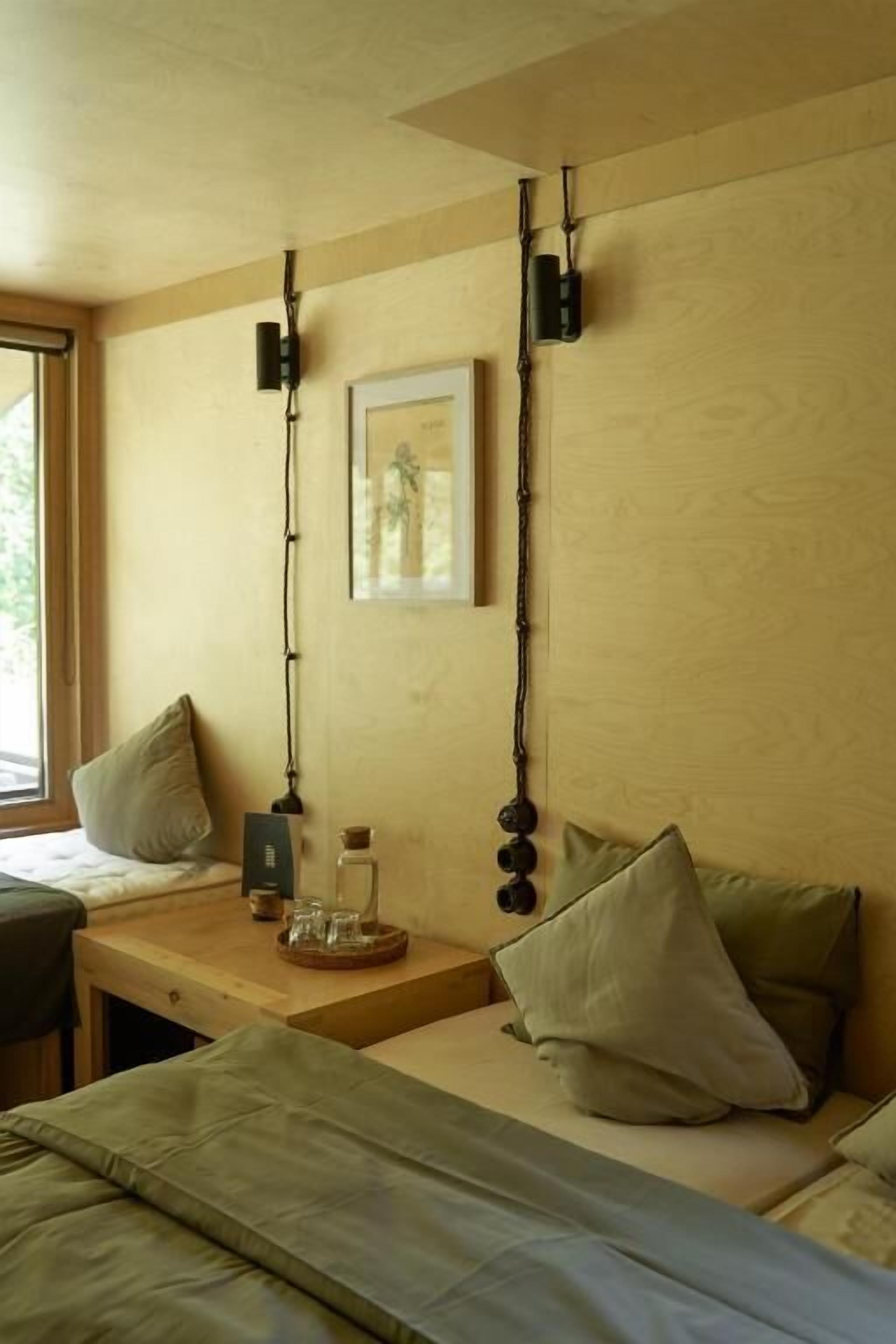 A room with a bed, a small table, a window, and a wall-mounted light fixture.