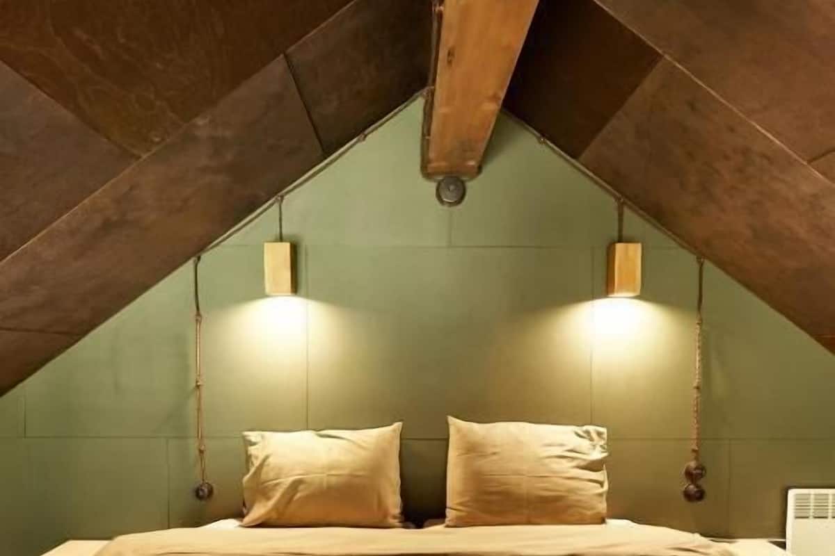 A bedroom with a sloped ceiling, a bed with beige bedding, two wall-mounted lights, and a white radiator.