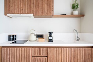 A modern kitchen with wooden cabinets, a white countertop, a kettle, a coffee maker, and a sink. - Volaka Luxury Suites `Sapphire` (Kos)
