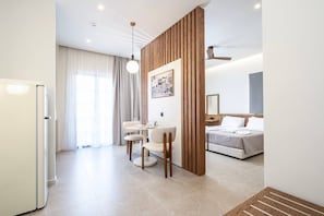A modern hotel room with a dining area, a bed with a headboard, and a wooden partition. - Volaka Luxury Suites `Sapphire` (Kos)