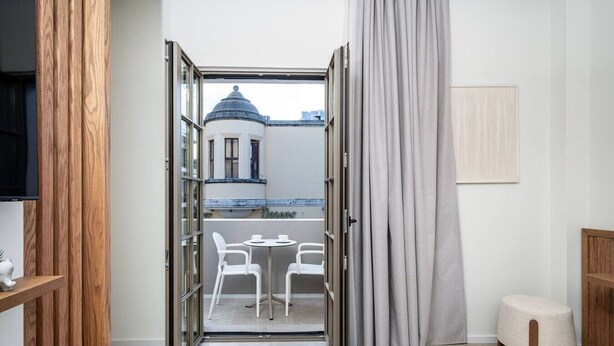 Ein Hotelzimmer mit Balkon, einem Essbereich mit Stühlen, einem Bett und einem Fernseher.