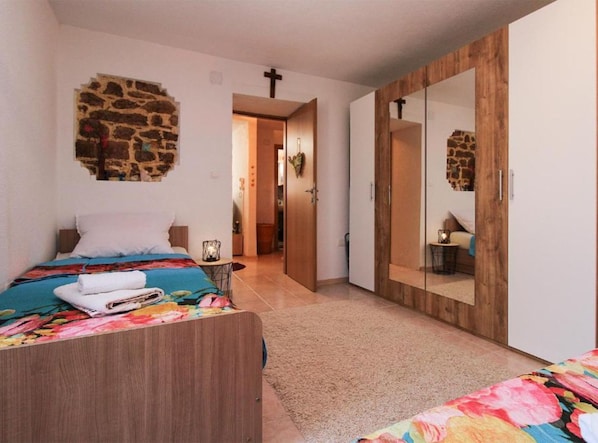 A bedroom with a bed, a nightstand, a mirror, and a door leading to another room.