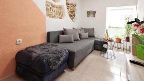 Una sala de estar con un sofá gris, un pequeño otoman, una mesa de centro y una pared con textura similar a la piedra.