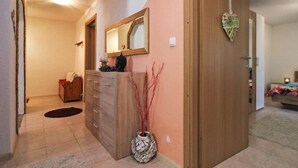 Un pasillo con puerta de madera, espejo, cómoda y un florero con ramas.