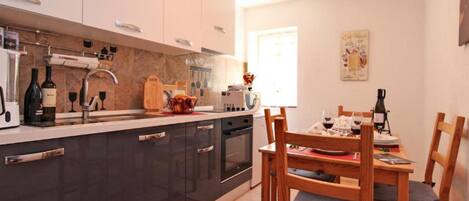 A modern kitchen with dark cabinets, a dining area with wooden chairs, and a window providing natural light.