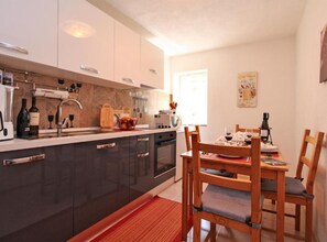 Una cocina moderna con armarios oscuros, un área de comedor con sillas de madera y un ventanal que proporciona luz natural.
