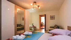 Un dormitorio con cama, armario, espejo, una mesa con flores y una puerta que da a otra habitación.