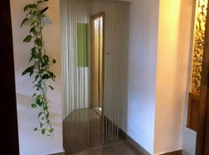 A hallway with a plant on the left, a striped curtain, and a stone wall on the right.