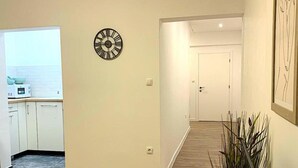 Un couloir avec une horloge, une porte et une plante.