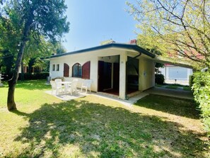 A single-story building with a covered patio, a small lawn, and a white fence. - Spacious Single House With Barbecue and Garden (San Michele al Tagliamento)