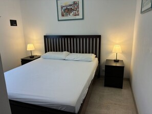 Un lit bien fait, avec du linge de lit blanc, deux tables de chevet avec des lampes, une tête de lit avec des lattes verticales et un tableau encadré au mur.
