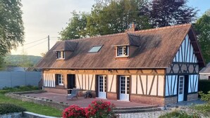 Una casa tradicional de entramado de madera con techo inclinado, un porche delantero y un pequeño jardín con flores rojas.