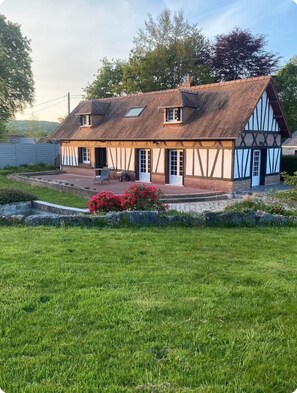 Ein traditionelles Fachwerkhäuschen mit geneigtem Dach, einer Veranda und einem kleinen Garten mit roten Blumen.