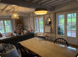 Een ruime kamer met een grote houten tafel, een ingebouwde bank en een hoog plafond met zichtbare balken.