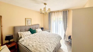 Un dormitorio con cama, mesitas de noche, una araña, cortinas y un cuadro en la pared.